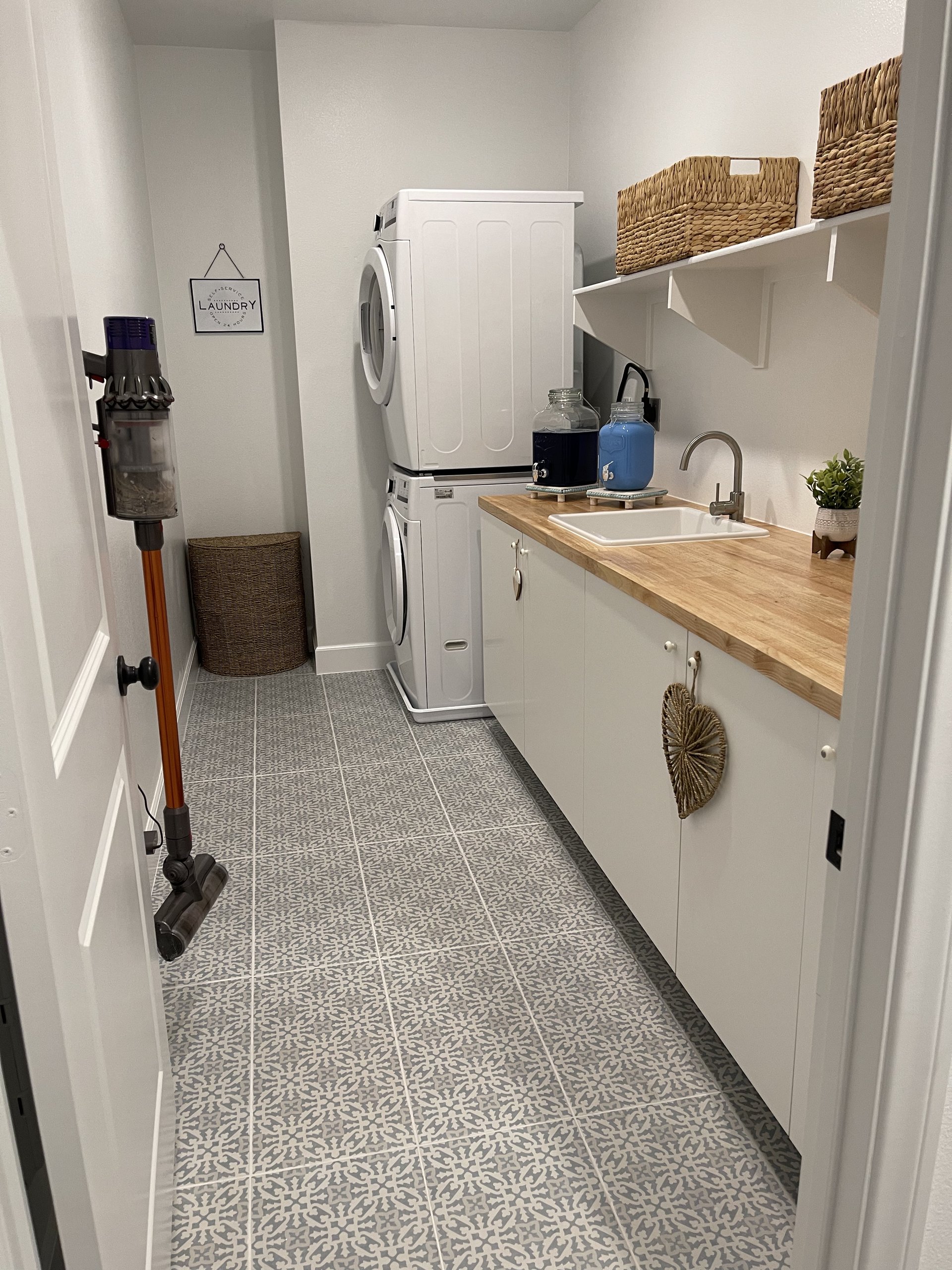 Finished laundry room with butcher block counter, stacked appliances, and patterned tile — Menifee, CA